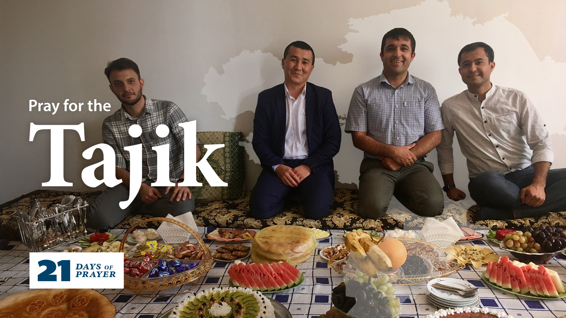 A group of four men sit around a spread of food: fruits, desserts, candy, and baked goods.